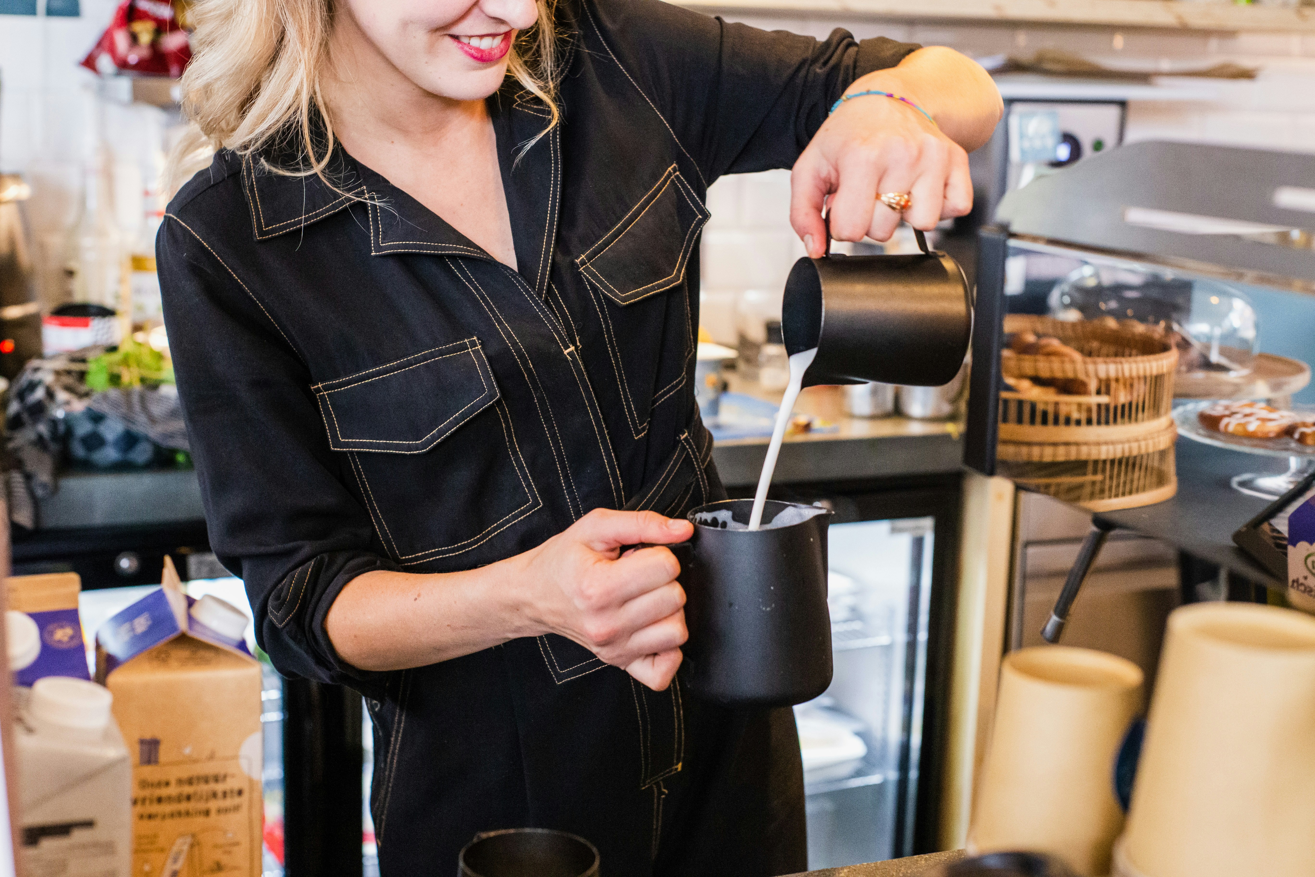 Barista pouring milk into a black cup