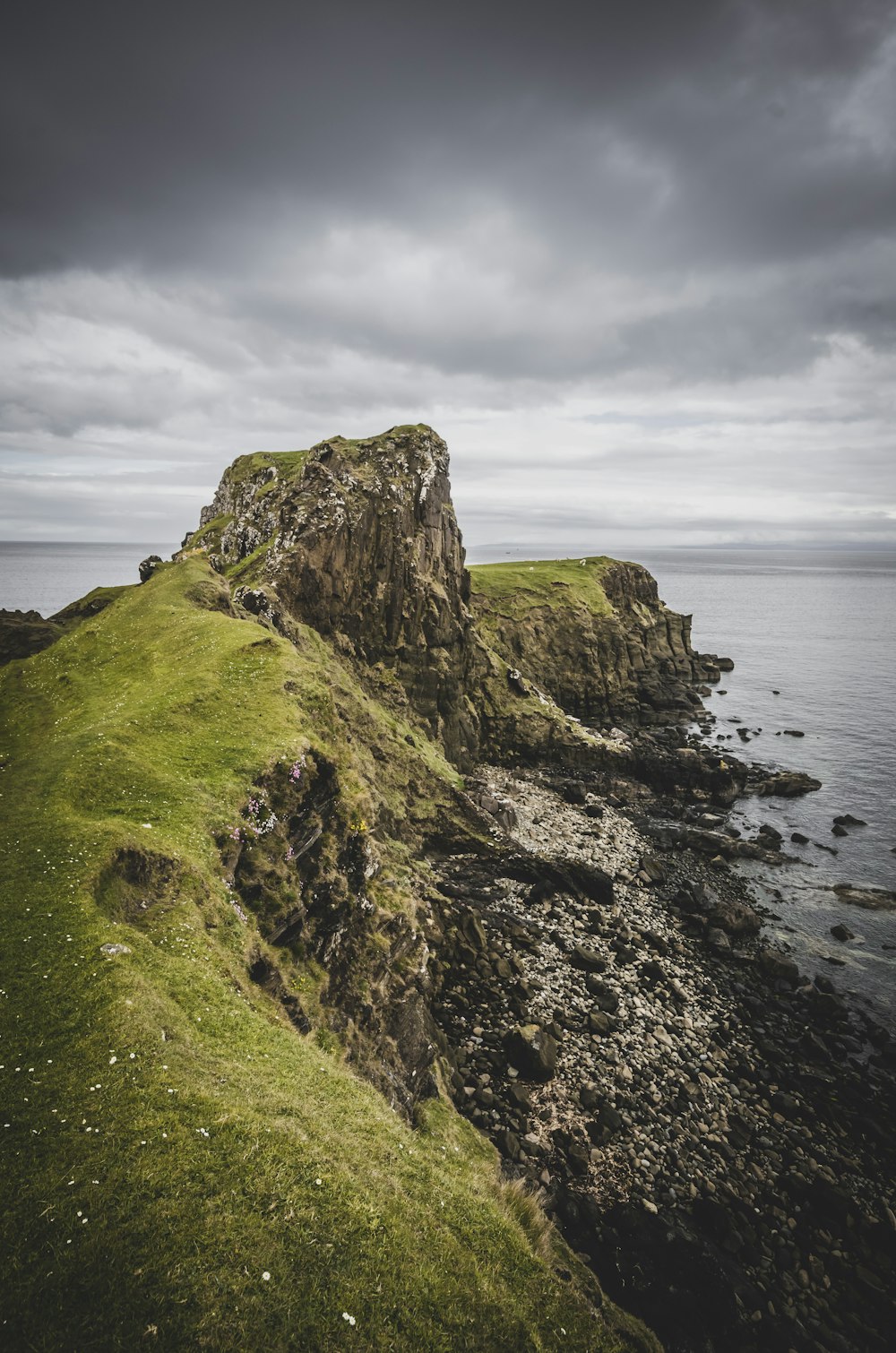 green and black rock formation beside sea under white clouds during daytime