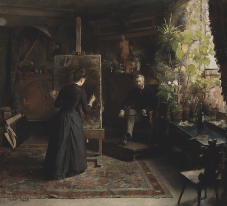 A dark, richly detailed art studio with an artist painting at an easel. The room is filled with natural light from a large window, highlighting the lush greenery of potted plants. A seated man observes the artist's work, surrounded by various objects including brushes, a table, and a patterned rug.