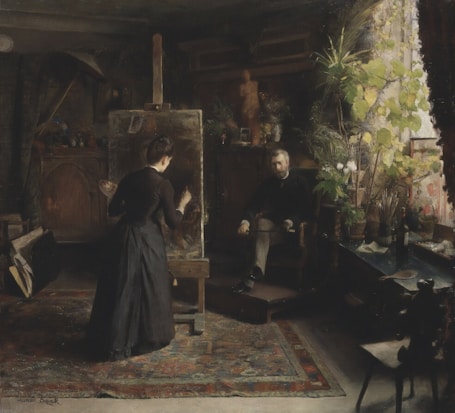 A dark, richly detailed art studio with an artist painting at an easel. The room is filled with natural light from a large window, highlighting the lush greenery of potted plants. A seated man observes the artist's work, surrounded by various objects including brushes, a table, and a patterned rug.