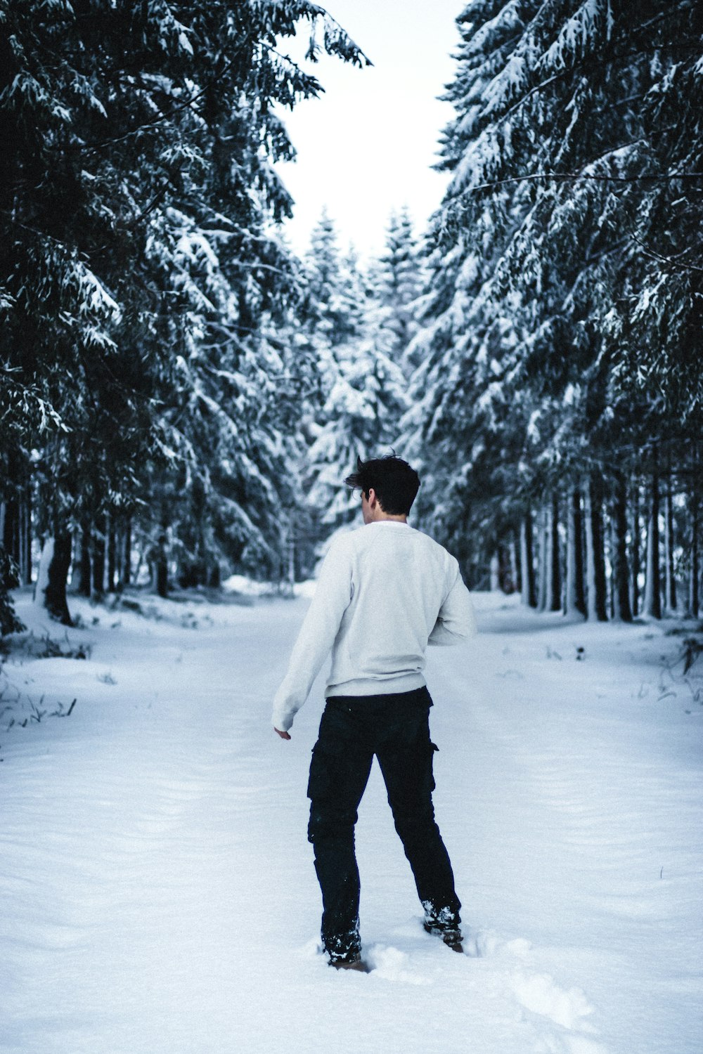homem de moletom branco e calças pretas andando no chão coberto de neve durante o dia