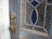 A close-up view of a weathered wooden door featuring a vintage doorknob and lock. The glass panel in the door is intricately patterned with floral designs and highlighted with blue stained glass inserts.