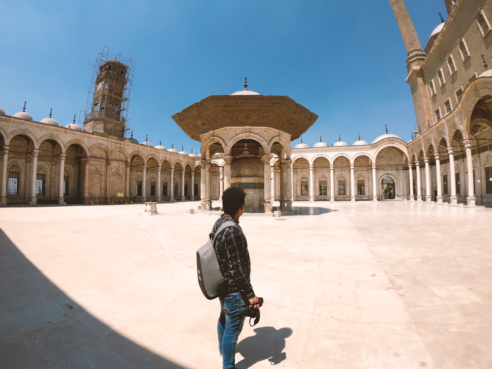 man in black jacket and blue denim jeans standing in front of brown concrete building during