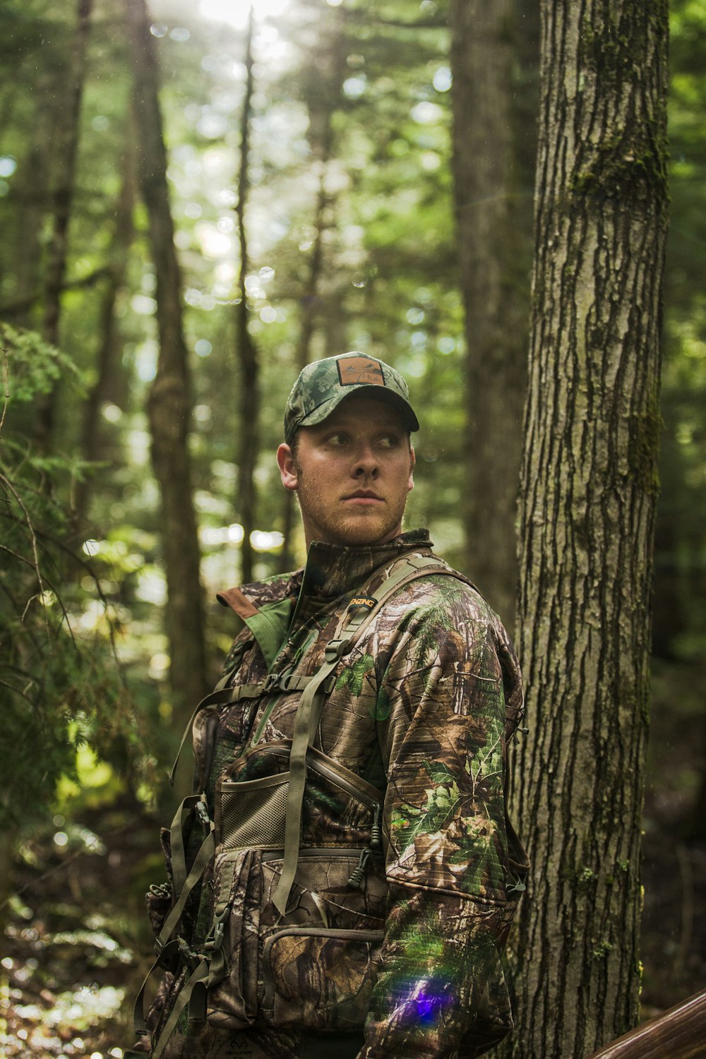 homme en veste de camouflage marron et vert debout près de l’arbre pendant la journée