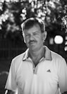 man in polo shirt standing near fence in grayscale photography