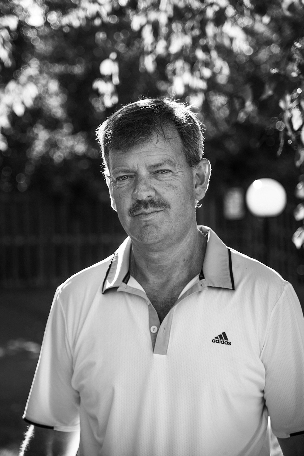 man in polo shirt standing near fence in grayscale photography