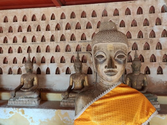 gold buddha statue in front of white concrete wall in Wat Si Saket Laos