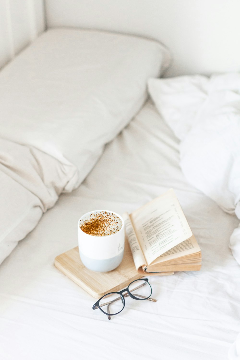 Taza de cerámica blanca en bandeja de madera marrón al lado del libro