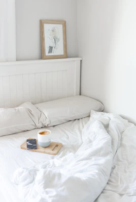 A calm bedroom corner featuring soft white linens and warm wooden furniture.