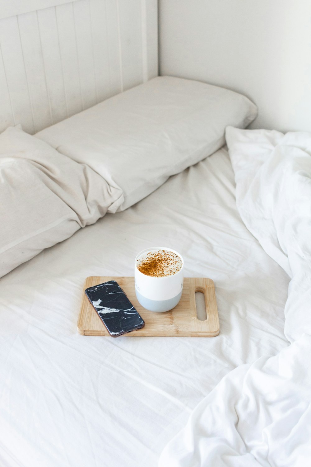 white ceramic mug on brown wooden chopping board beside white bed pillow