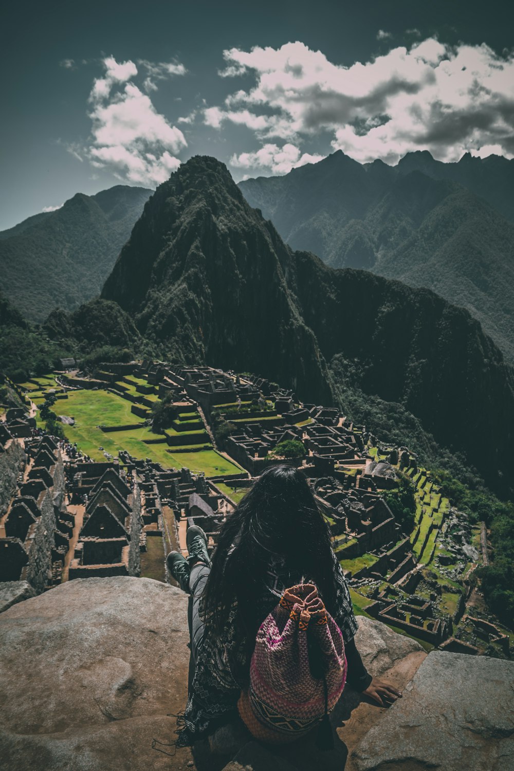 person in black and white plaid shirt sitting on rock looking at the mountains during daytime