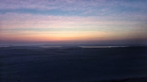A serene desert landscape with endless dunes under a fiery twilight sky.