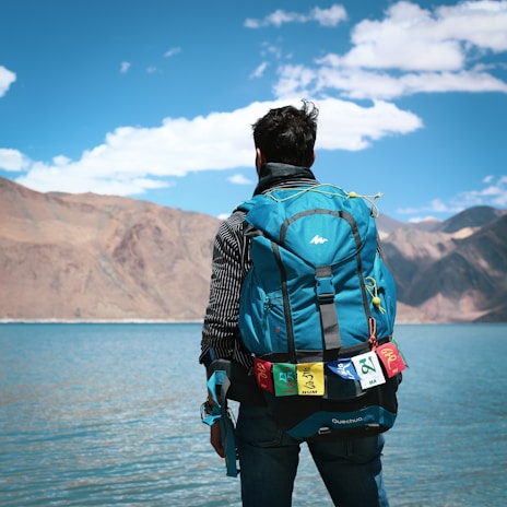 A backpacker adjusting their ryvo windbreaker while standing beside a serene mountain lake.