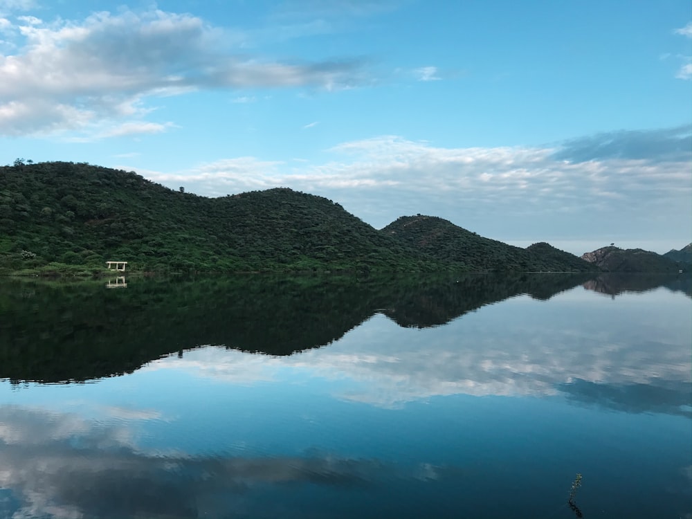 green mountain beside body of water under blue sky during daytime