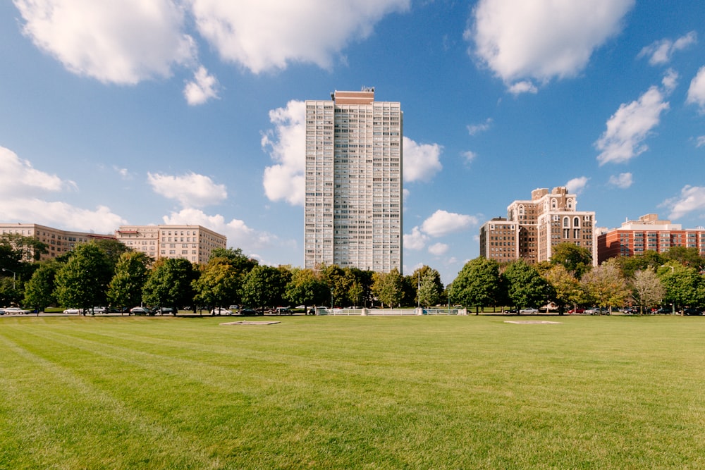 green grass field near city buildings under blue sky during daytime