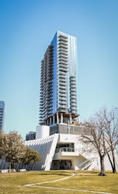 A sleek modern skyscraper with green landscaping in front, under a clear blue sky.