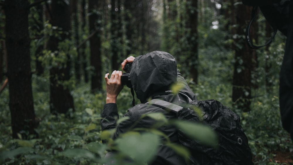 낮에 숲에서 검은 DSLR 카메라를 들고 있는 검은 재킷을 입은 남자