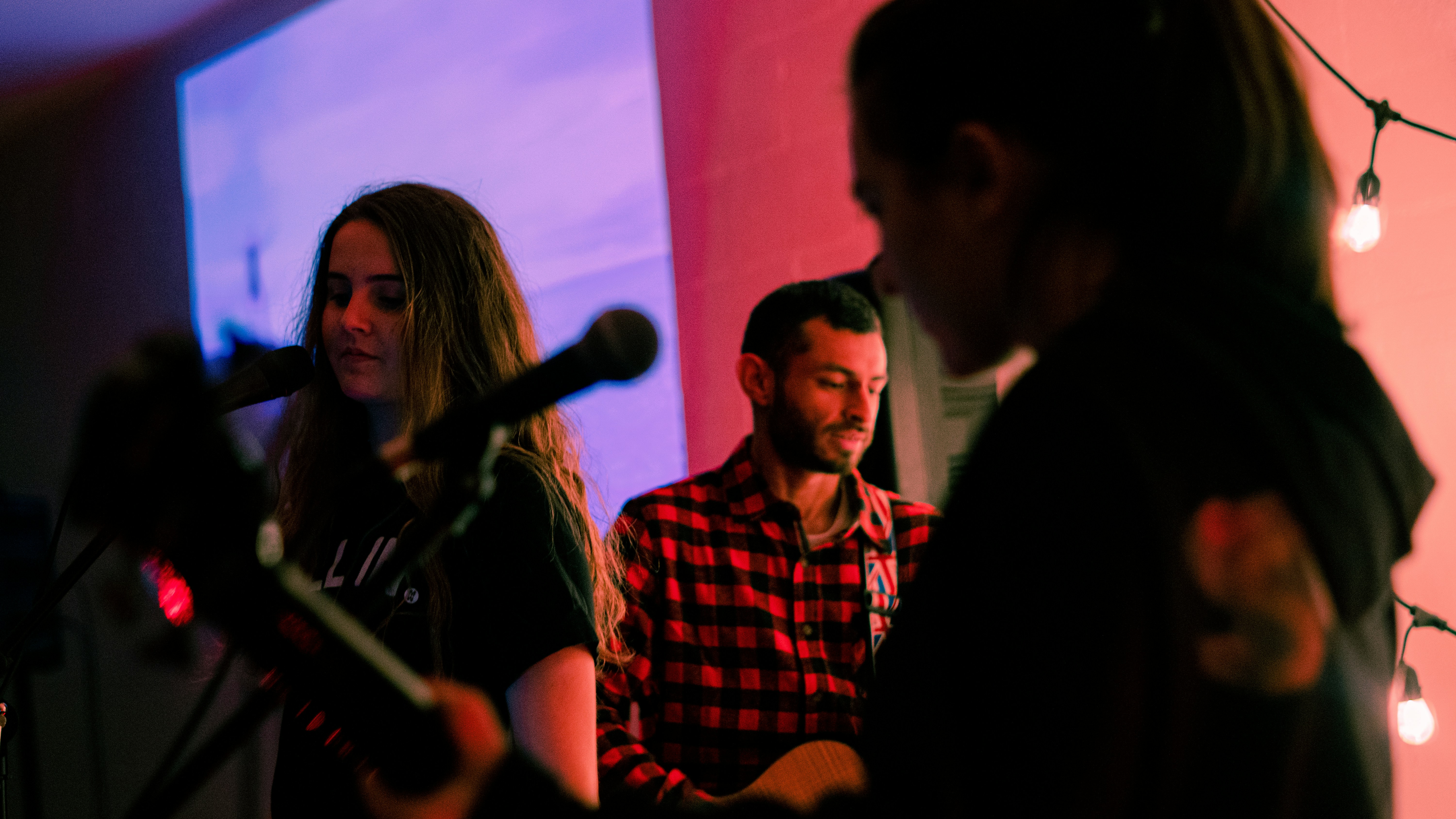 man in red and white plaid dress shirt singing beside woman in black dress