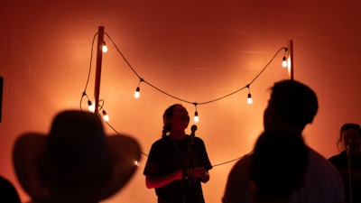 An intimate scene of Agnes speaking on stage with warm lighting and an attentive audience smiling.