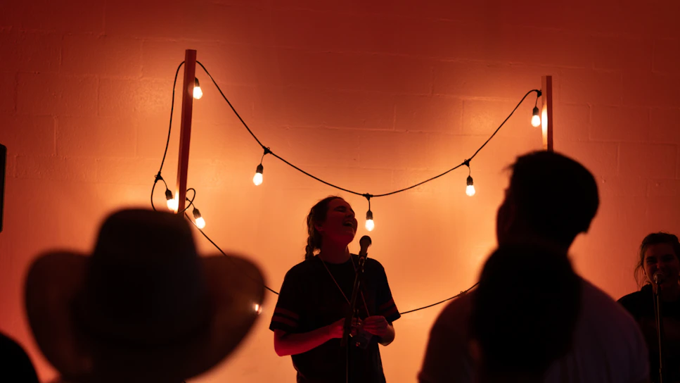 A lively open mic night with a diverse crowd enjoying performances under warm string lights.
