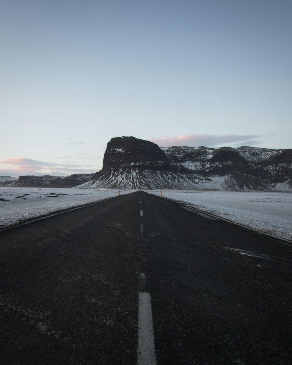Route asphaltée noire près d’une montagne enneigée pendant la journée