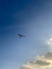 Airplane soaring through a clear blue sky with soft clouds.