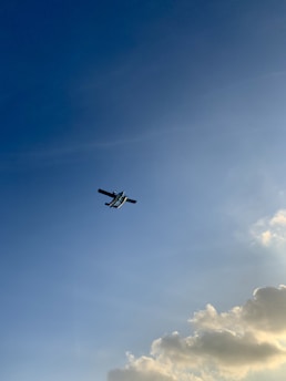 Airplane soaring through a clear blue sky with soft clouds.