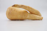 Close-up of a sliced parsnip revealing its creamy interior against a backdrop of green herbs.
