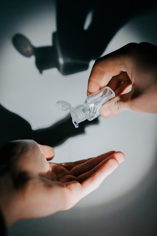 A bottle of alcohol gel with hands applying sanitizer in the background.