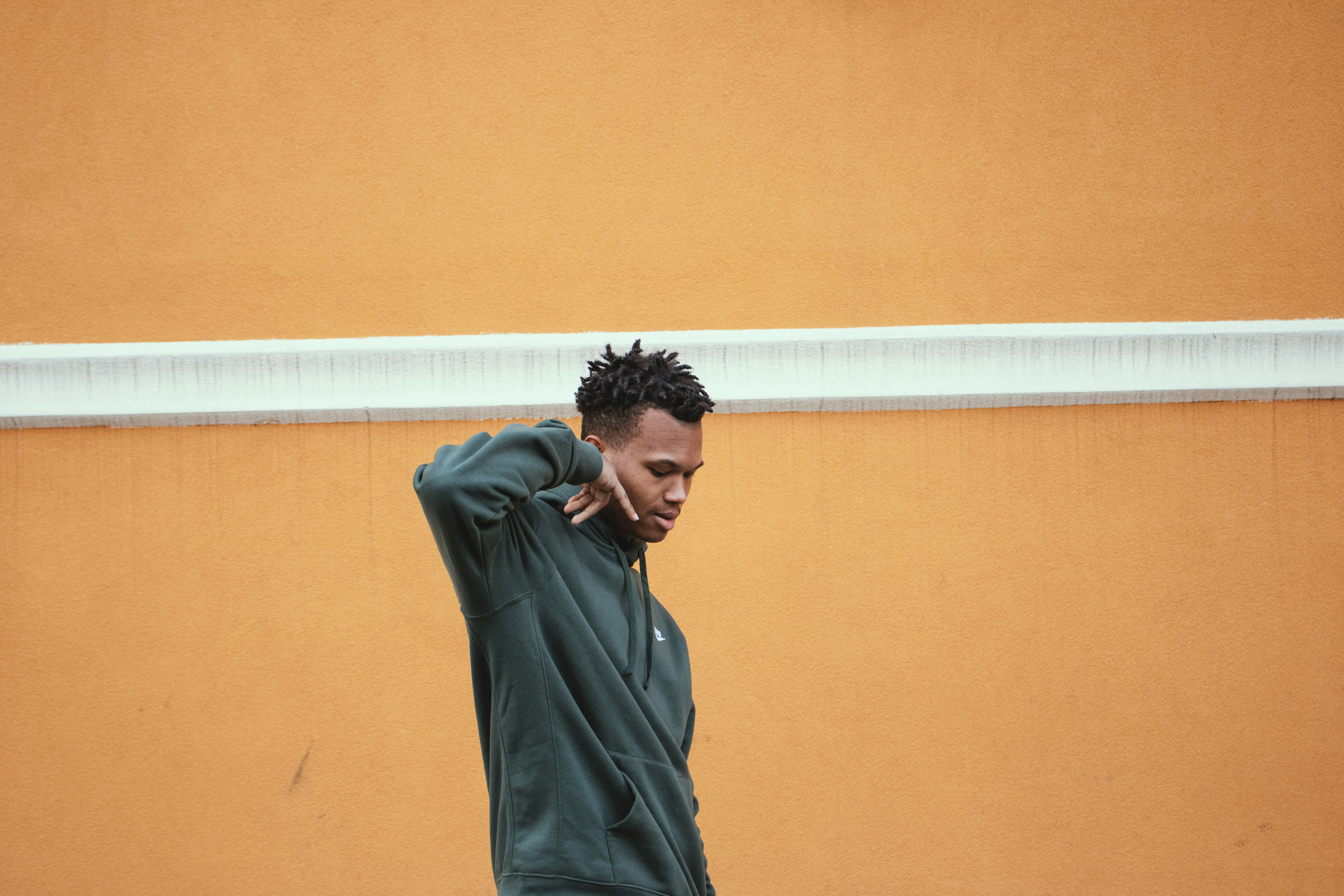 man in gray long sleeve shirt standing beside brown wall