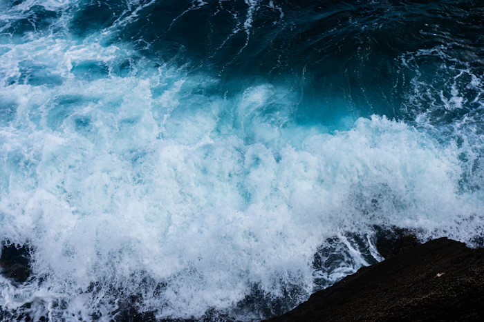 Waves crashing against dark rugged rock along the East End coastline