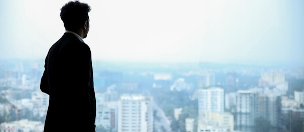 man in black suit standing on top of building looking at city buildings during daytime