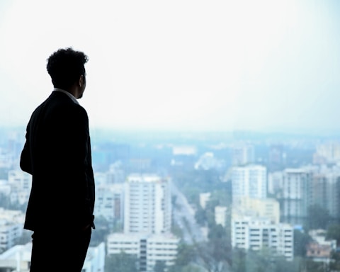 man in black suit standing on top of building looking at city buildings during daytime