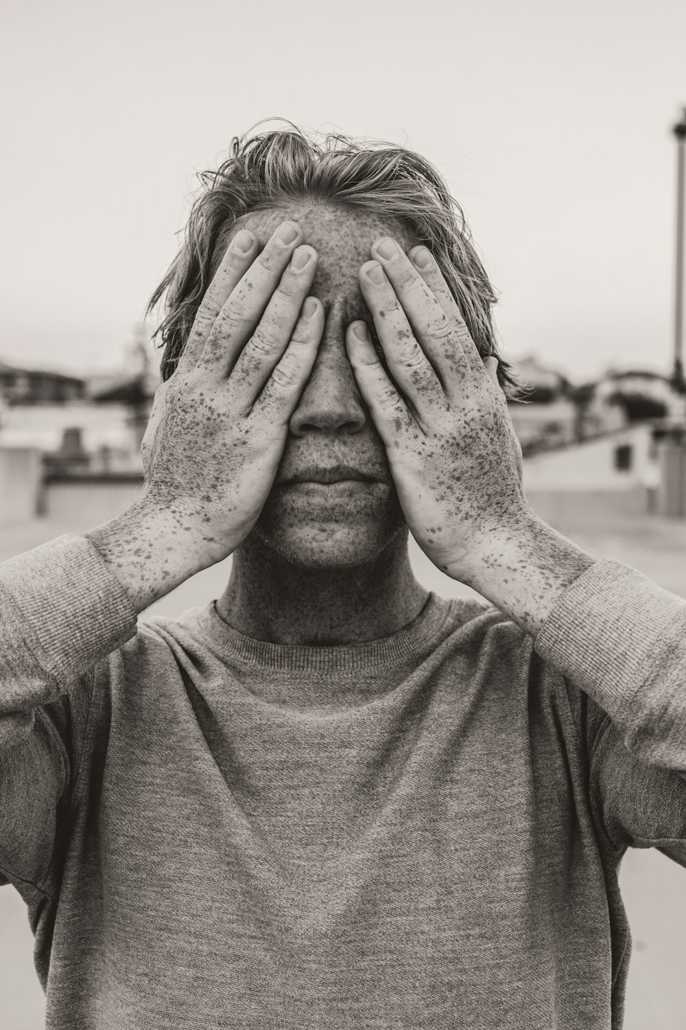 man in gray crew neck shirt covering his face with his hands