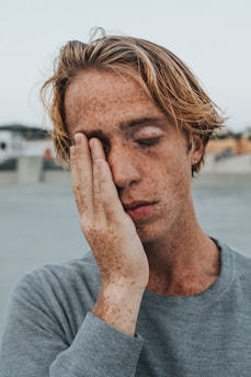 man in gray crew neck shirt covering his face with his hand