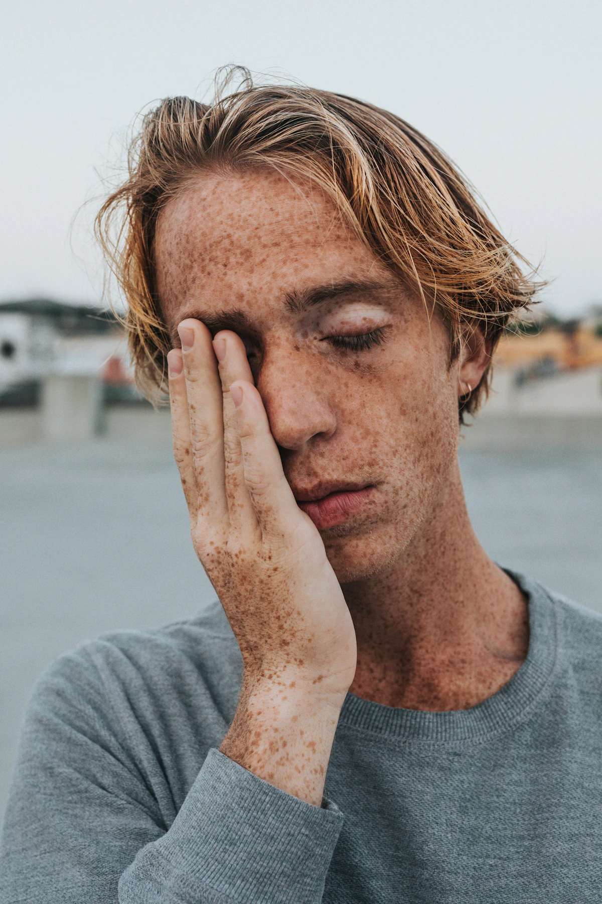 Man in a gray shirt covering his face with his hand, illustrating the early warning signs of testosterone deficiency like fatigue and low motivation.