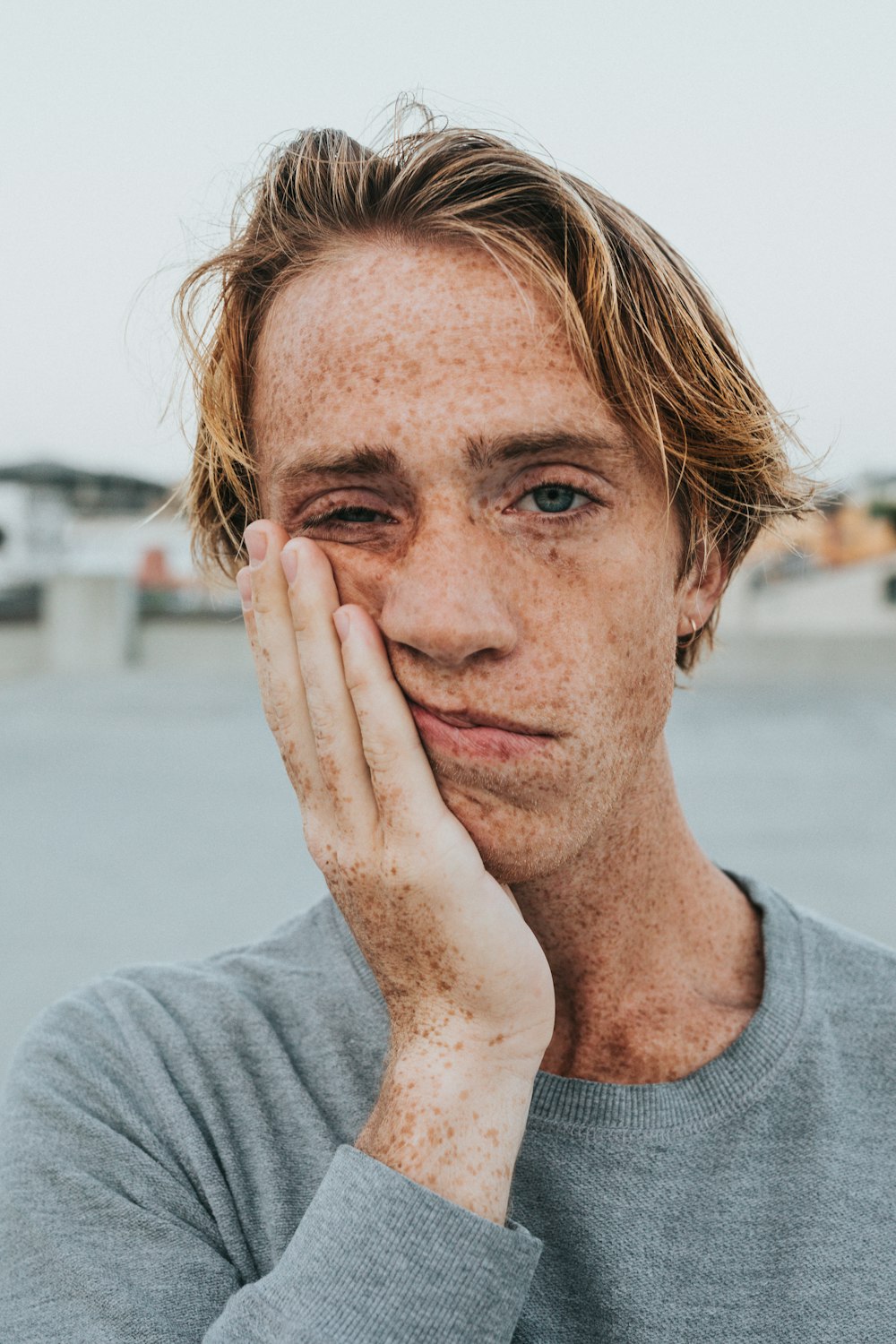 uomo in camicia girocollo grigia con mano sul viso