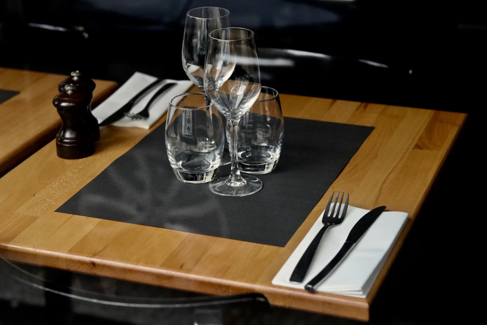 Wooden table set with wine glasses and forks arranged neatly on black placemat