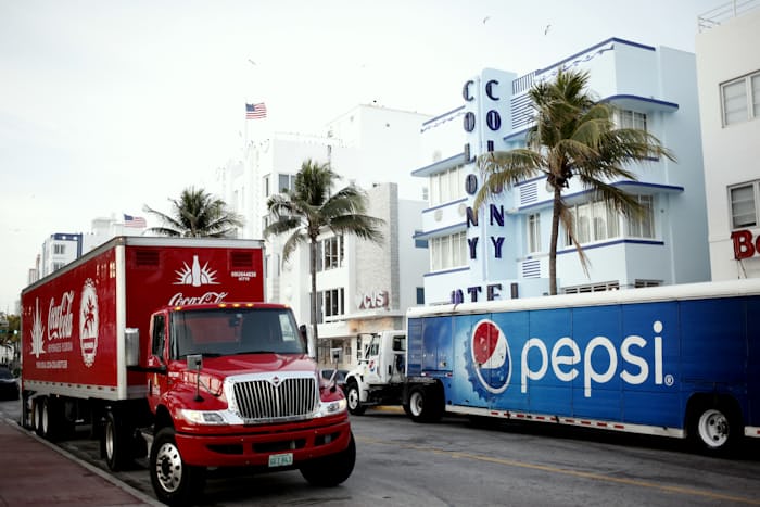 A Cocacola truck next to a Pepsi truck; red color a part of both brands