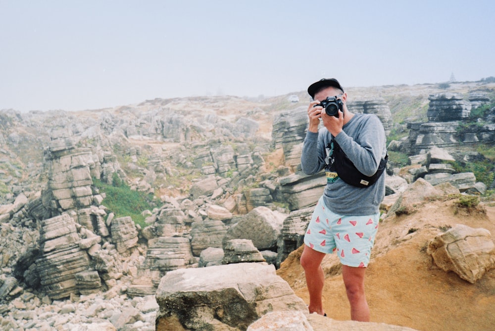 man in grey shirt and blue shorts standing on rock formation during daytime