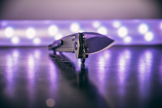 A sleek, modern knife placed on a reflective surface with a blurred background of circular lights creating a soft glow. The focus is on the detailed texture of the knife handle and its sharp blade.