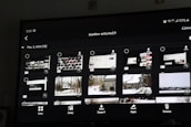 A digital screen displaying a photo gallery interface with thumbnail images. The interface includes options like 'View', 'Jump', 'Import', 'Apps', and 'Delete'. The thumbnails show a mixture of screenshots and landscape photos, some of which depict snowy scenes and cabins.