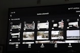A digital screen displaying a photo gallery interface with thumbnail images. The interface includes options like 'View', 'Jump', 'Import', 'Apps', and 'Delete'. The thumbnails show a mixture of screenshots and landscape photos, some of which depict snowy scenes and cabins.