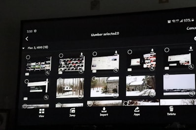 A digital screen displaying a photo gallery interface with thumbnail images. The interface includes options like 'View', 'Jump', 'Import', 'Apps', and 'Delete'. The thumbnails show a mixture of screenshots and landscape photos, some of which depict snowy scenes and cabins.