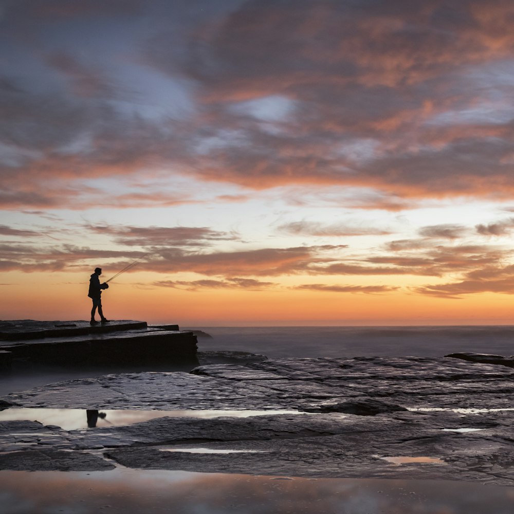 silhouette of person standing on beach during sunset