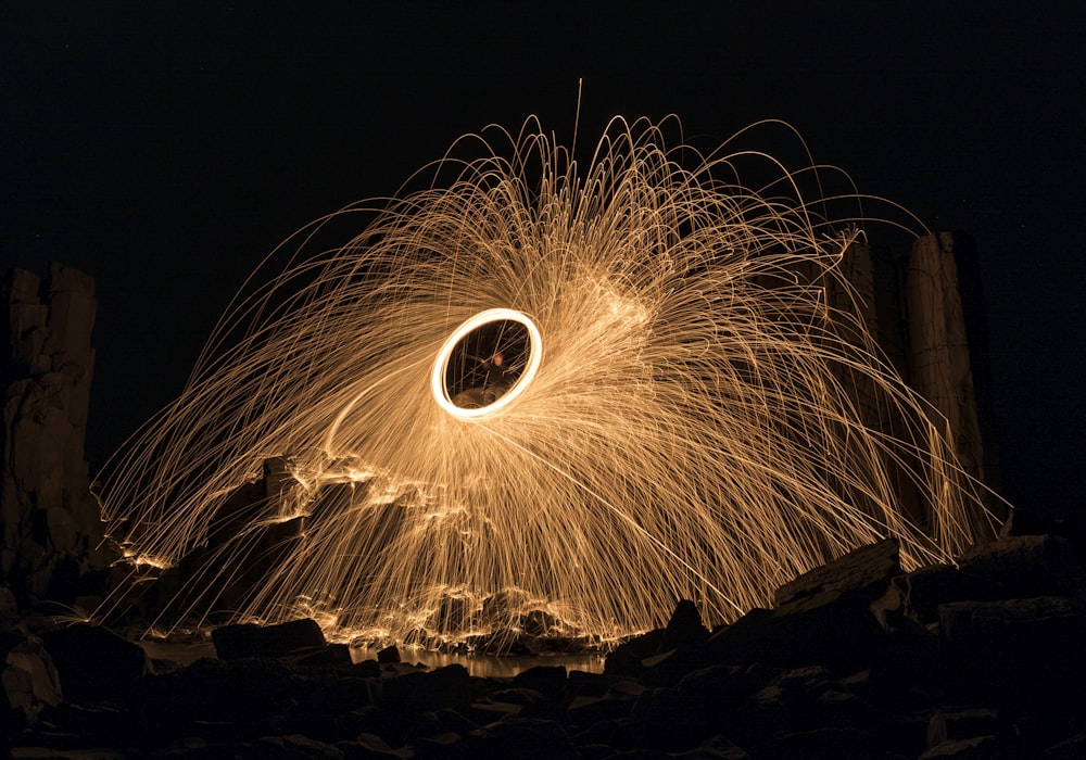 steel wool photography of person standing on brown sand during nighttime