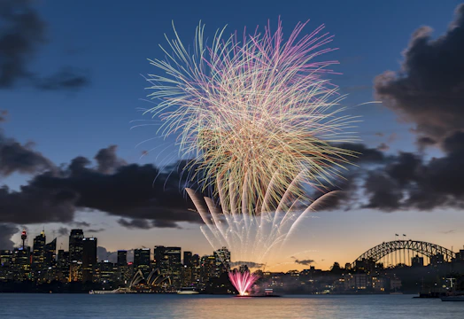 Vibrant fireworks exploding in a choreographed pattern over a city skyline at dusk.