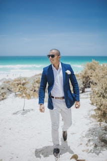 man in blue suit standing on white sand near body of water during daytime