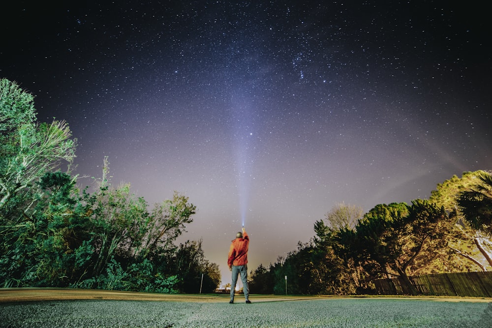 星空の夜の下、灰色のコンクリートの小道に立つ赤いシャツの男