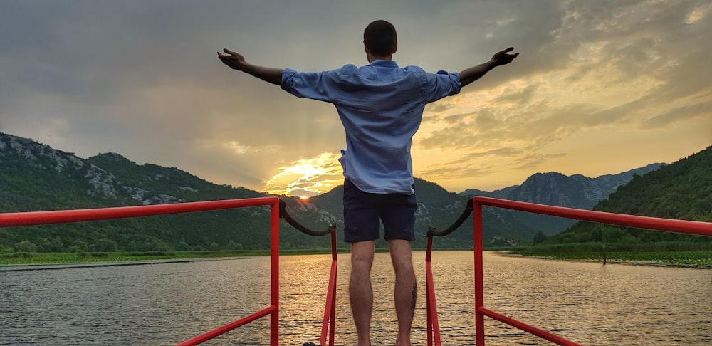 man in white shirt and black shorts standing on red metal railings during daytime